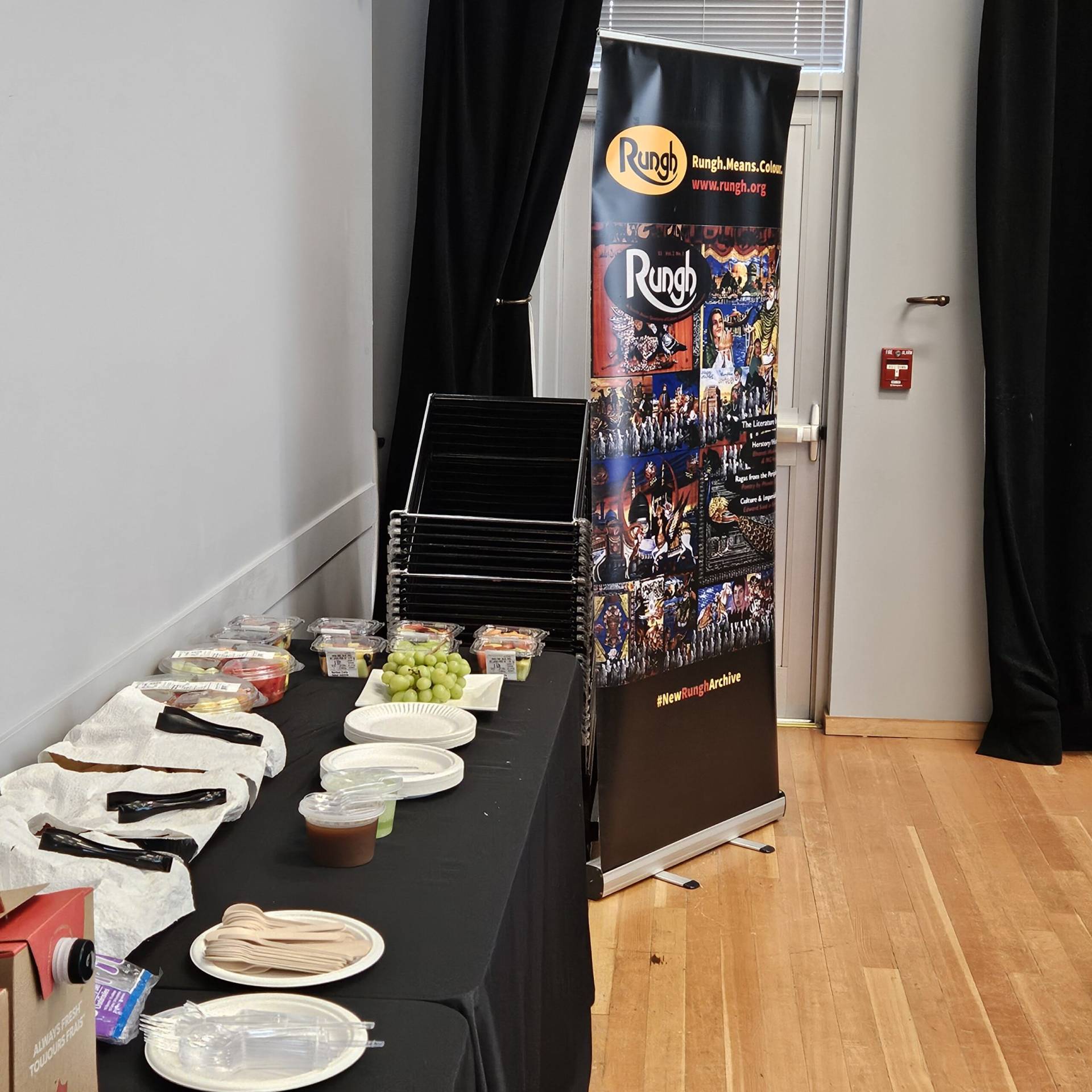 Diverse cultural event setup with food and Rungh promotional banner for community storytelling and arts.