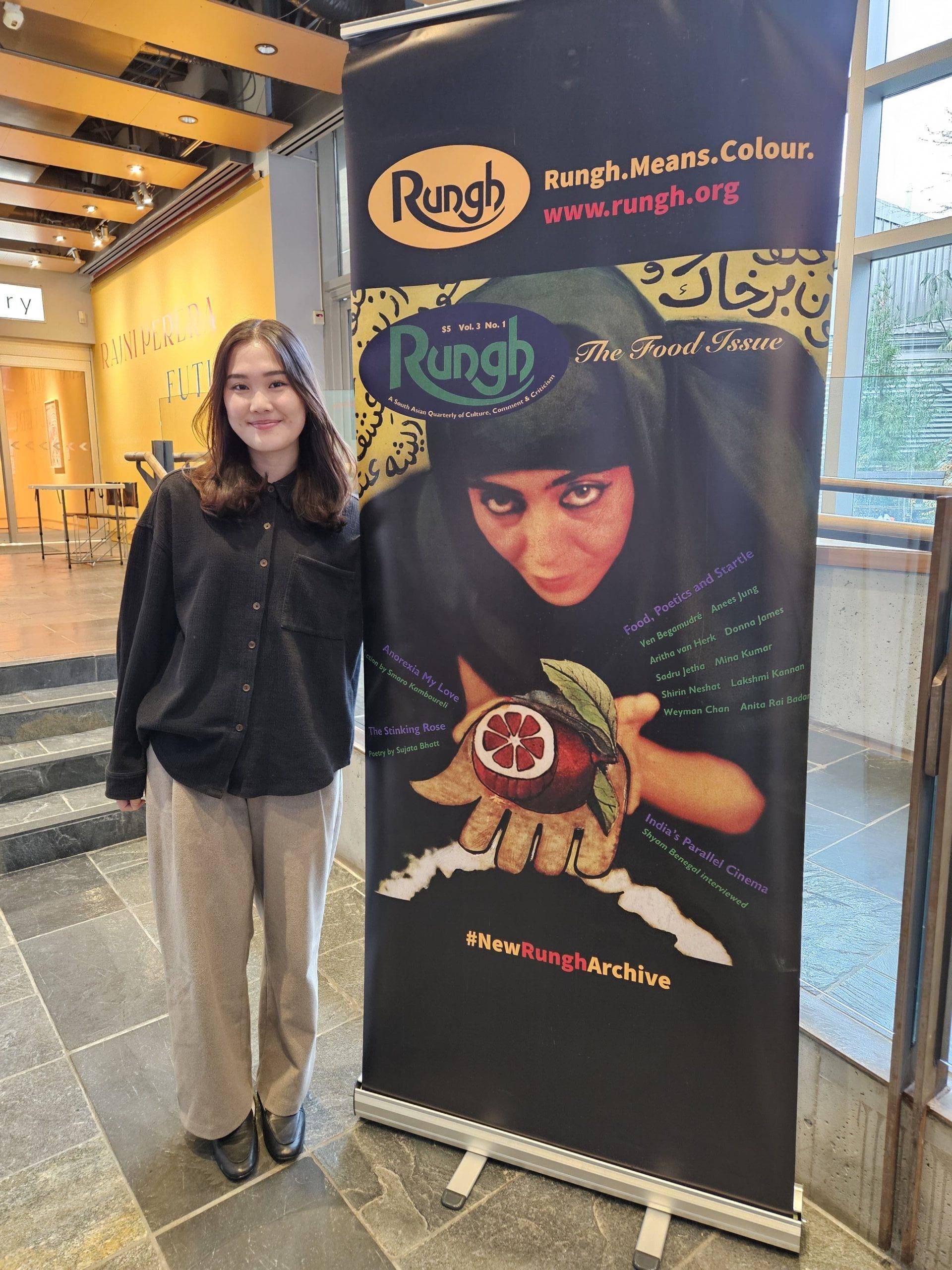 Thoughtful woman standing next to a colorful Rungh magazine display promoting Asian food and culture.