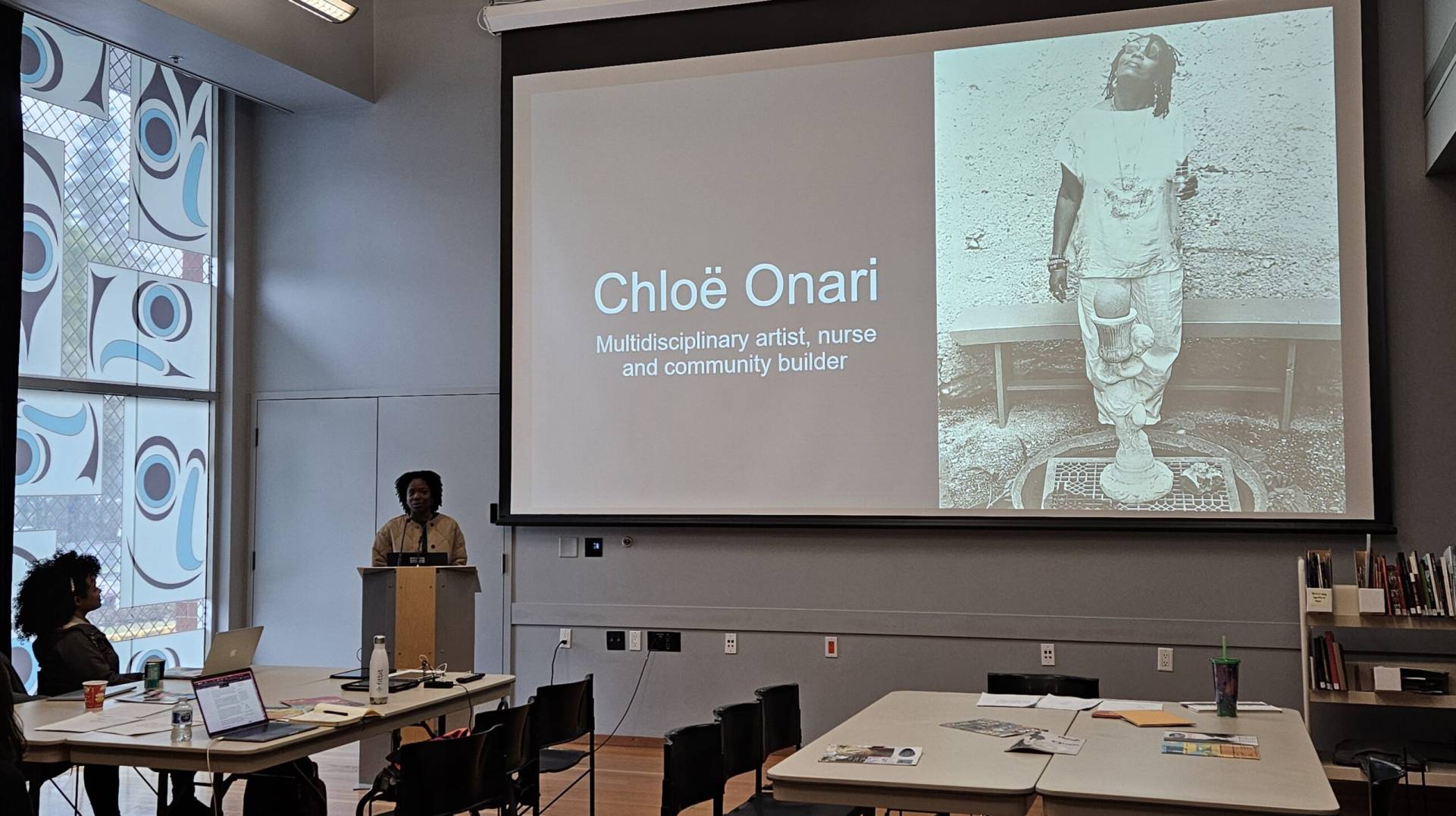 Multidisciplinary artist Chloë Onari giving a presentation in a modern library or gallery space.