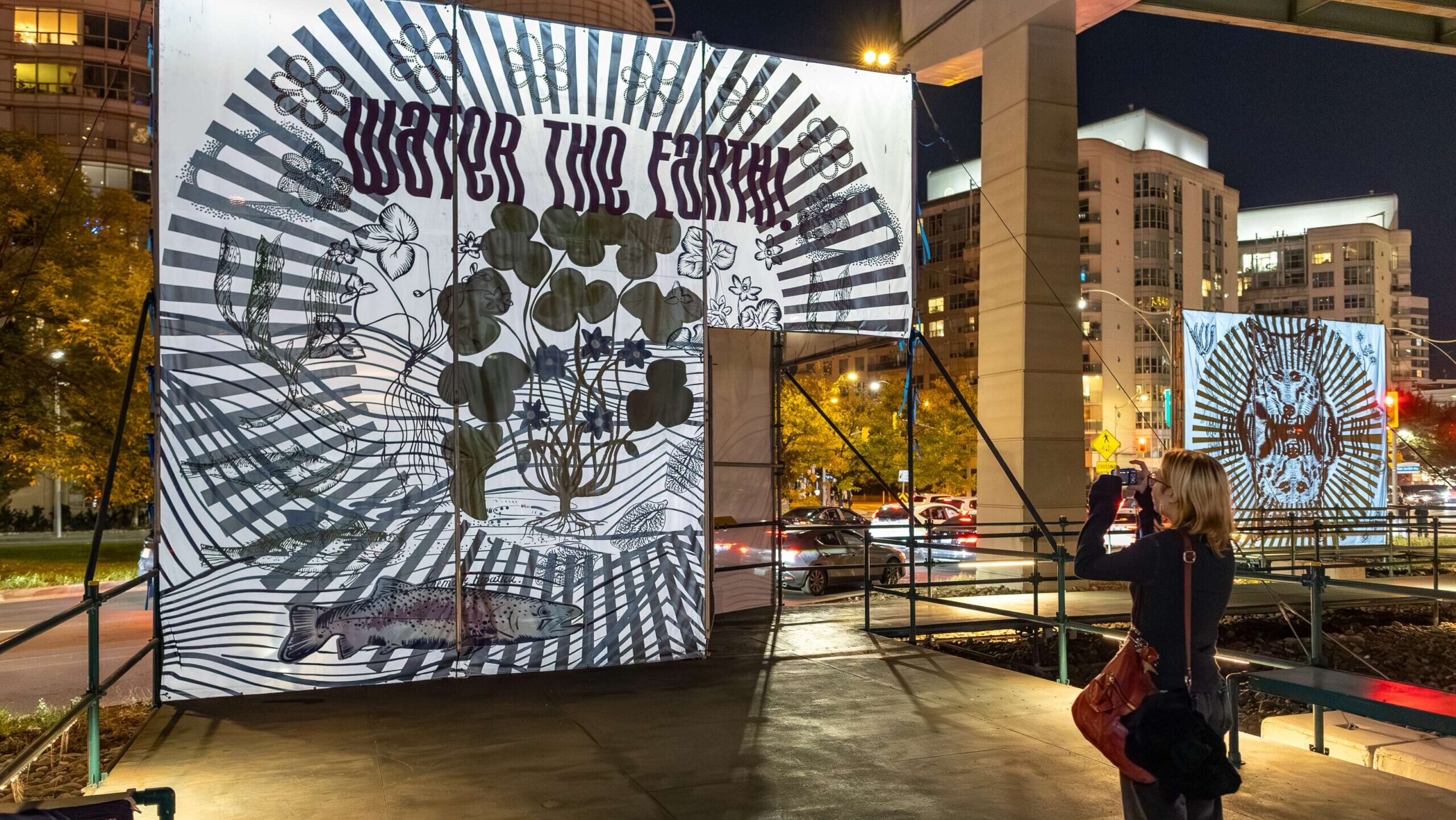 Bright outdoor art installation featuring a large screen with intricate black-and-white illustration.