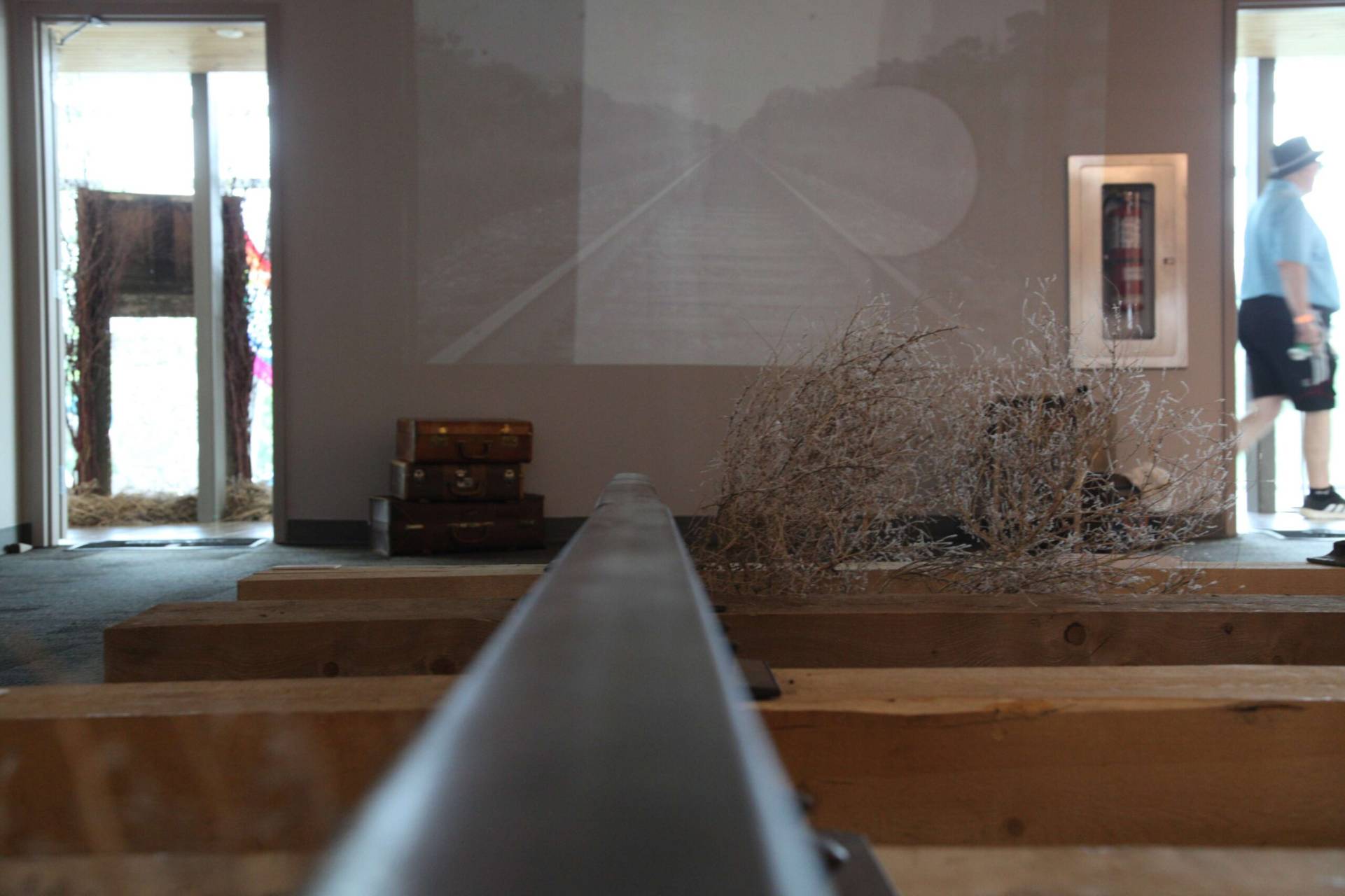 An art installation featuring a long metal rod extending into the distance, with wooden benches and.