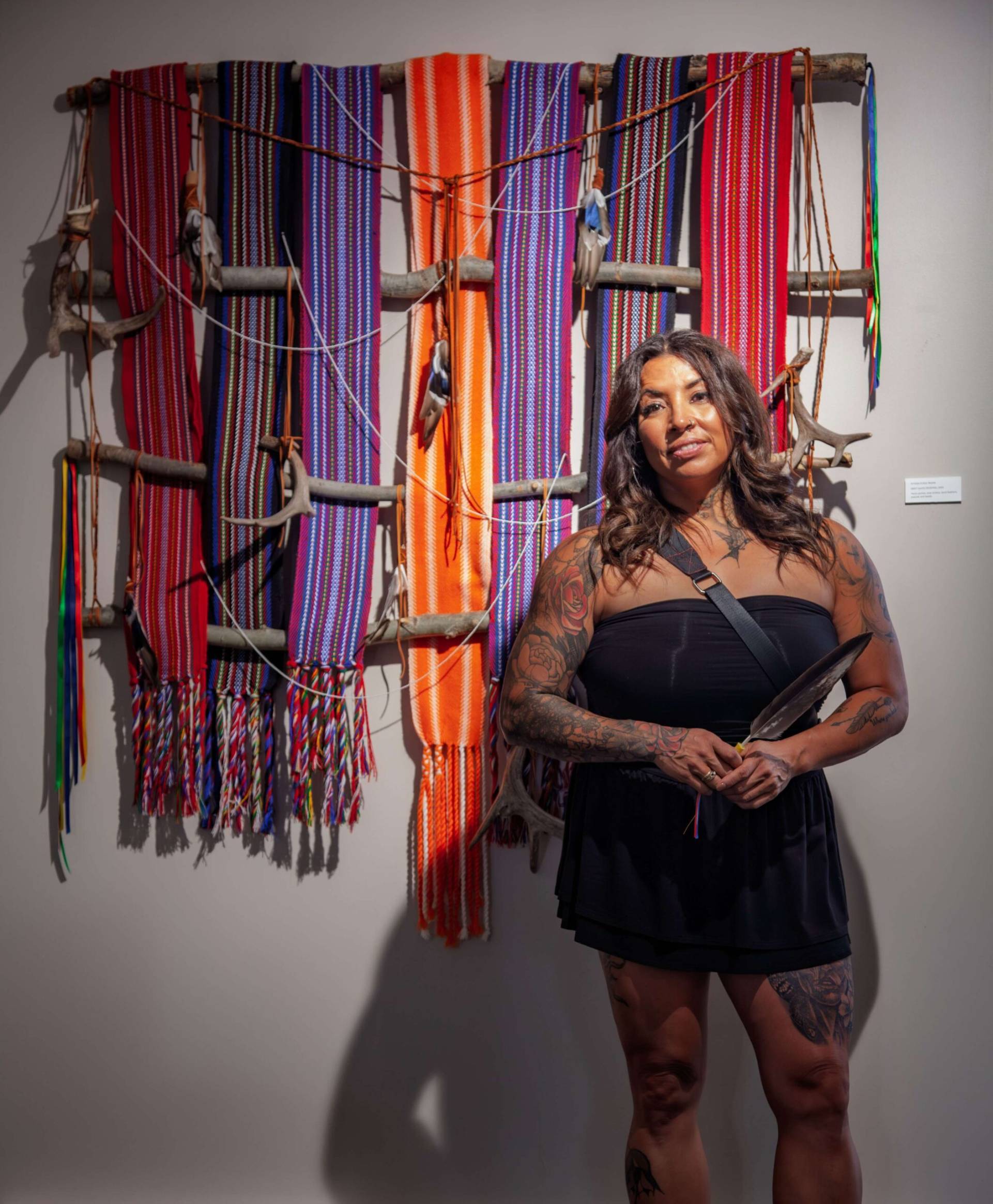 Indigenous woman standing in front of colorful woven textile art piece.
